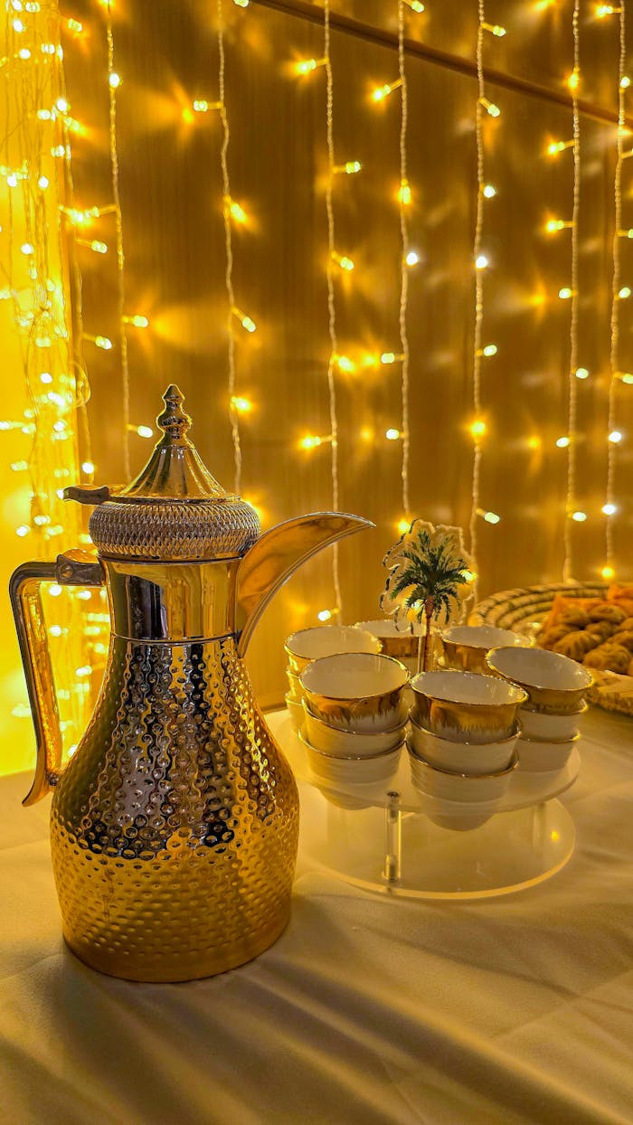 Home Gold coffee pot and cups with festive lights, perfect for luxury events and celebrations.